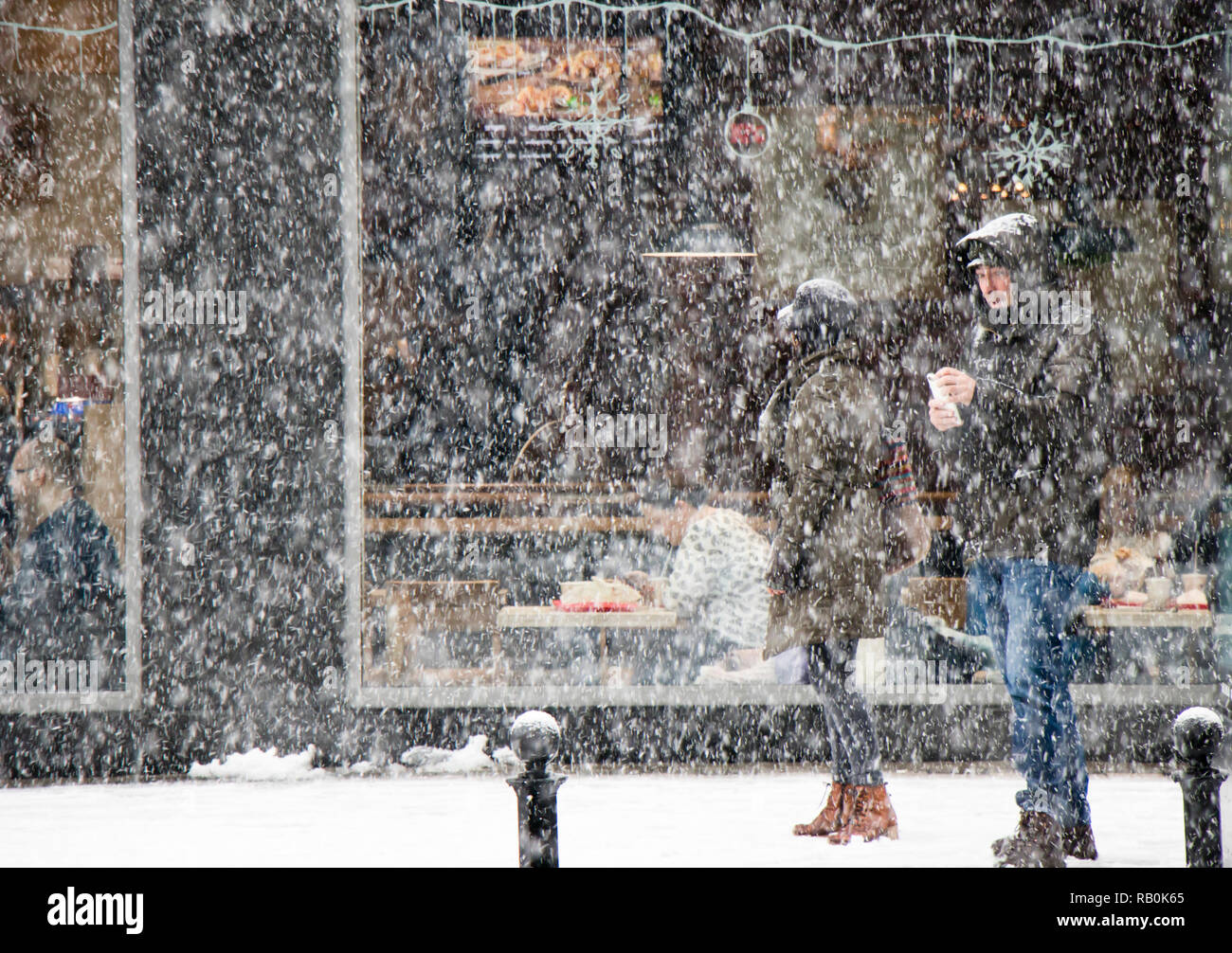 Belgrade, Serbie - 15 décembre 2018 : Couple Walking city street à de fortes chutes de neige et les personnes mangeant dans la fenêtre d'un restaurant derrière eux Banque D'Images