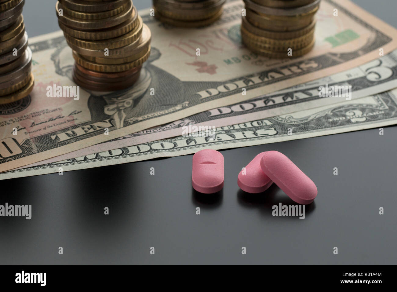 Trois comprimés, pilules roses avec des dollars et des piles de pièces de monnaie sur l'arrière-plan. Notion de frais médicaux Banque D'Images