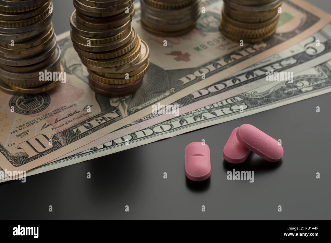 Pilules roses, des comprimés, des médicaments avec des dollars et des piles de pièces de monnaie sur l'arrière-plan. Notion de frais médicaux Banque D'Images