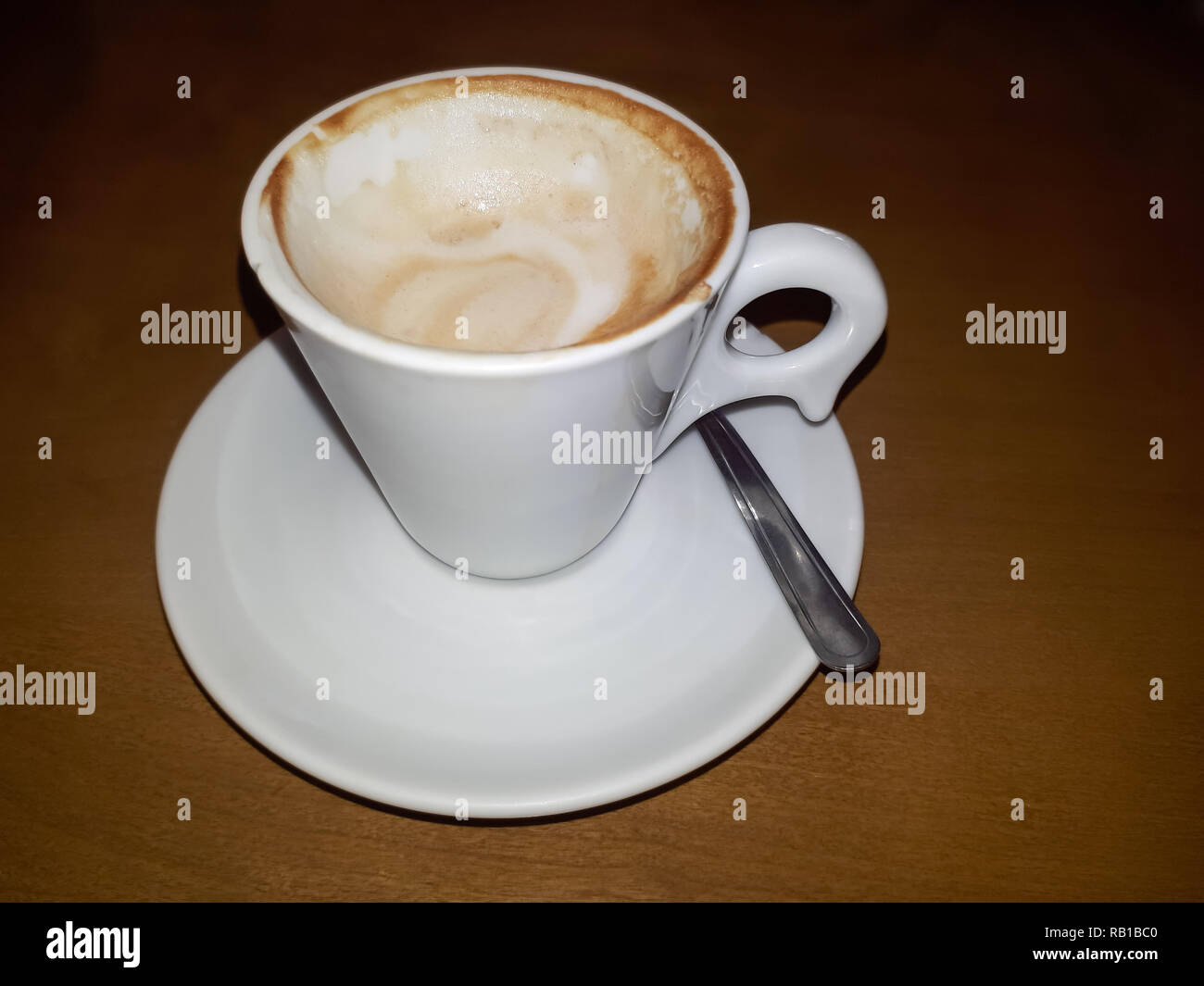 Un livre blanc et rempli tasse de café sur une soucoupe avec une cuillère à café à côté et un fond boisé assombrir Banque D'Images
