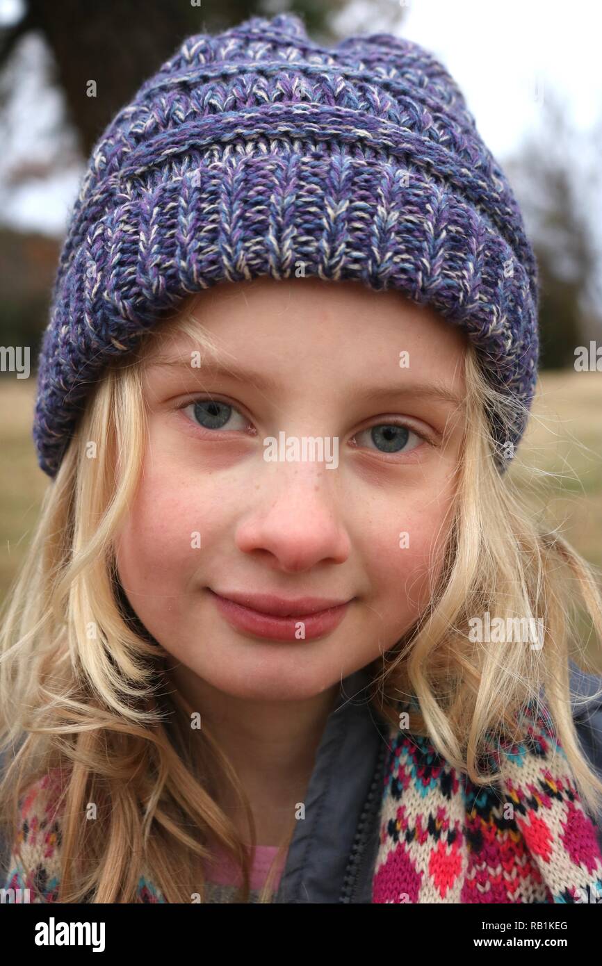 Portrait d'une jeune fille blonde aux yeux bleu portant un chapeau beanie pourpre dans le froid Banque D'Images