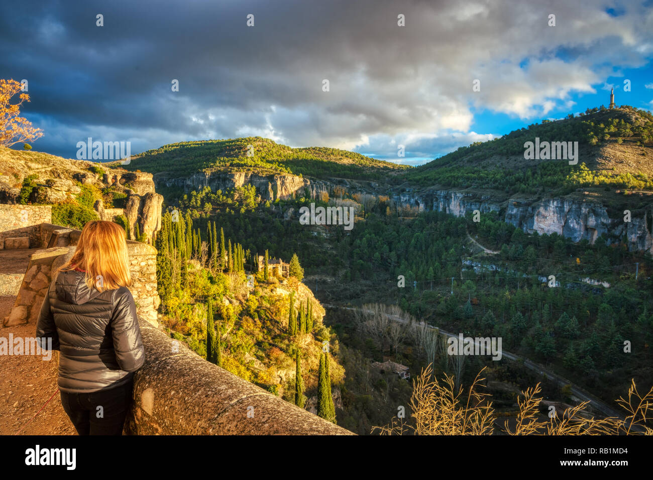 Une femme blonde à la recherche du haut château domaine de la Cuenca Espagne vers un canyon rocheux avec de vieux bâtiments, de grands conifères et moody nuages Banque D'Images