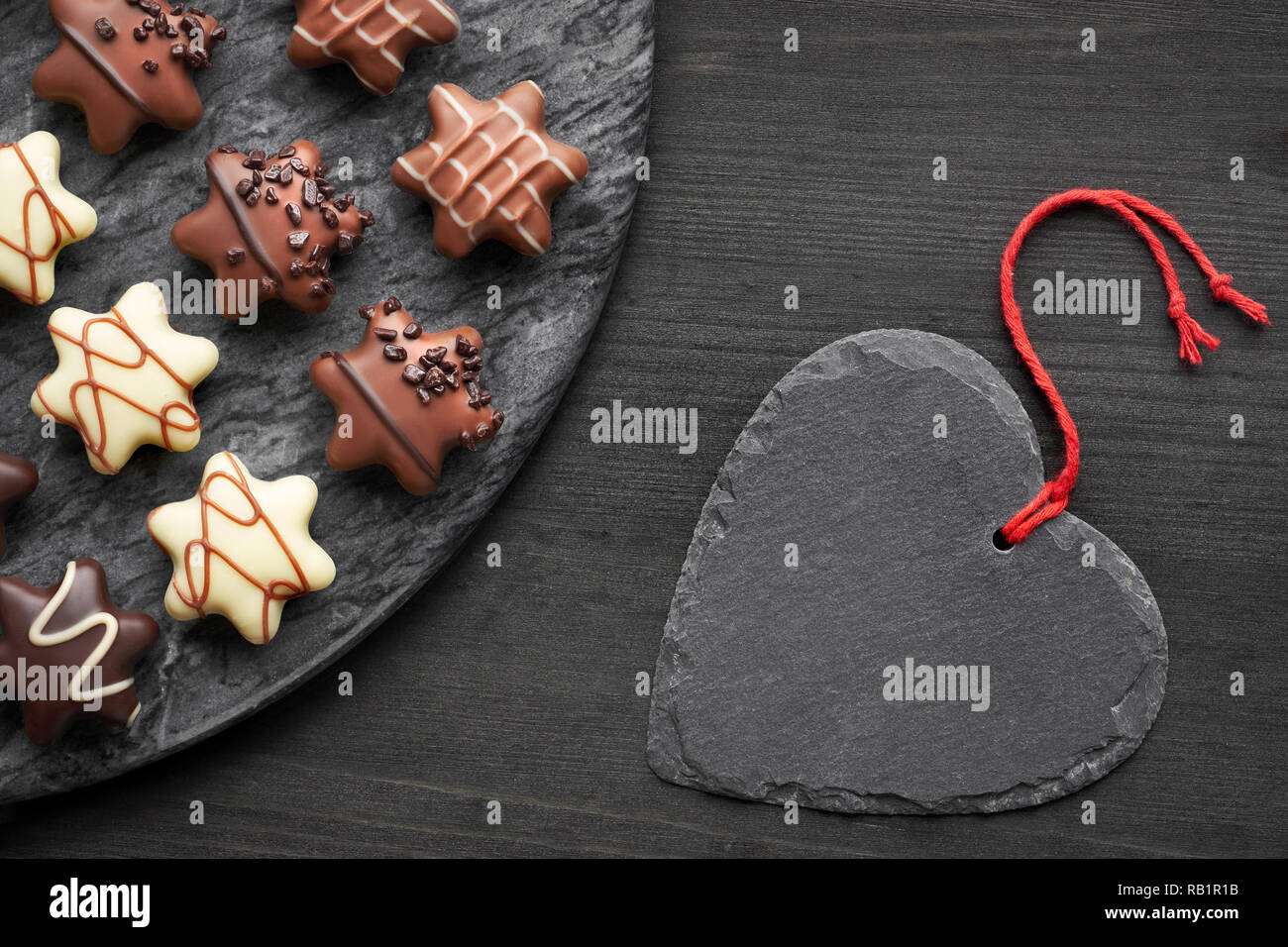 Chocolats en forme d'étoile sombre sur fond noir texturé avec ardoise coeur Banque D'Images