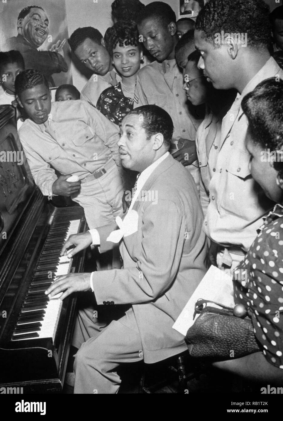 Le musicien de jazz américain Duke Ellington joue du piano pour un groupe d'hommes et femmes, Hartford, Connecticut, 1942. Chanteuse de jazz Joya Sherrill, qui a chanté avec Ellington thorughout la plupart des années 1940, se dresse au centre arrière (elle porte une perle neckace). Une affiche de Ellington est sur le mur. Banque D'Images