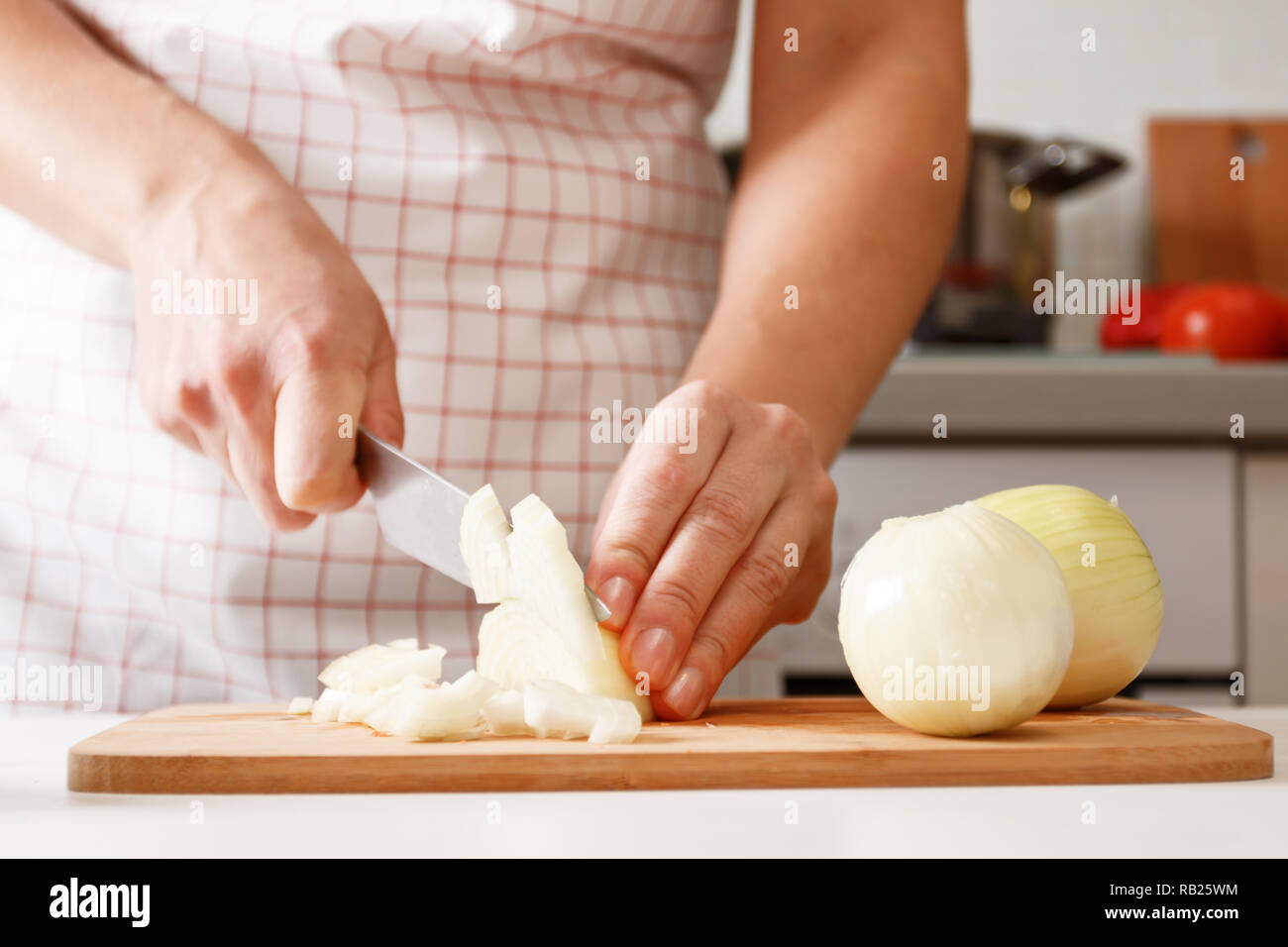 Femme cuisiner à la maison dans la cuisine, la coupe des oignons sur une planche de bois. Les aliments frais et sain. Close-up Banque D'Images