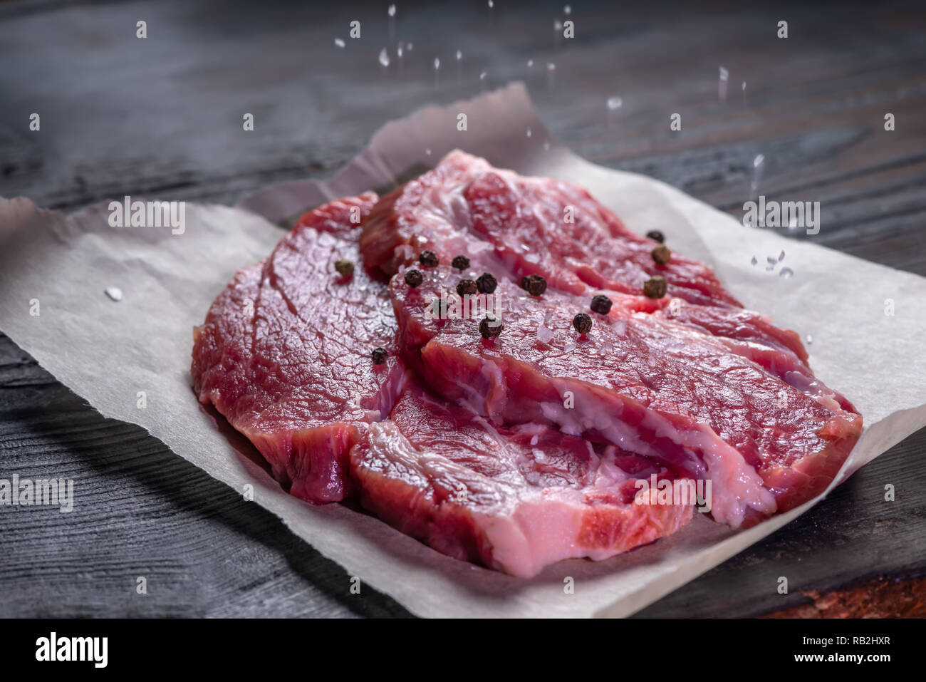 Partie de la viande de porc désossé frais strewing de sel et de poivrons sur table en bois, Close up Banque D'Images