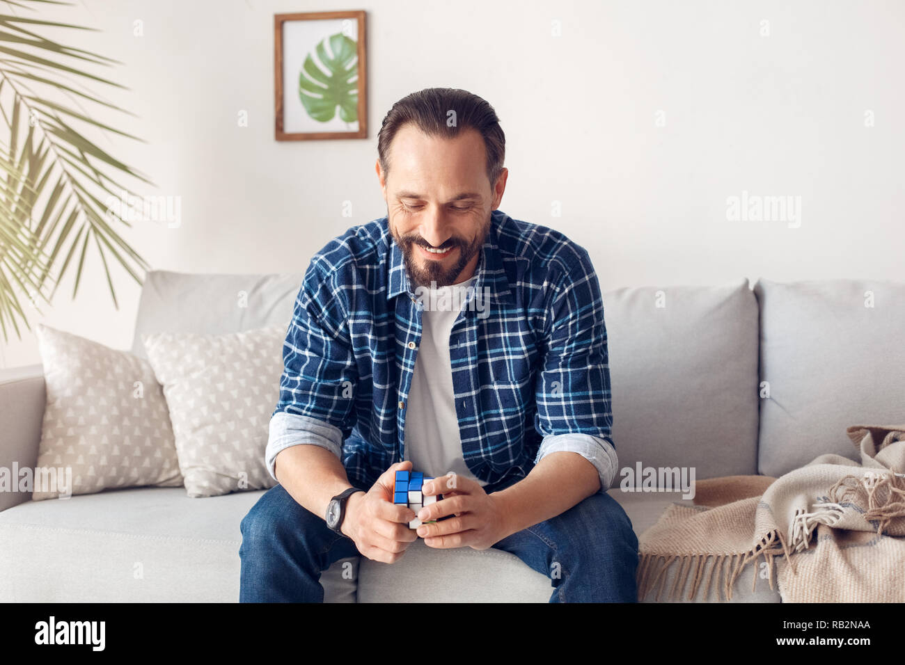 L'homme seul à la maison assis sur le canapé en combinaison sur rubik's cube joyeuse Banque D'Images