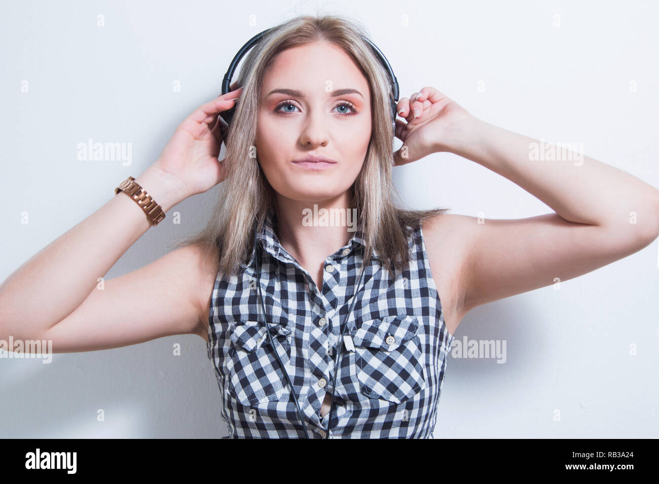 Belle jeune fille en chemise à carreaux avec des écouteurs et smart phone profiter de la musique à la maison, moitié du corps, portrait. Mur Blanc, youth music concept. Banque D'Images