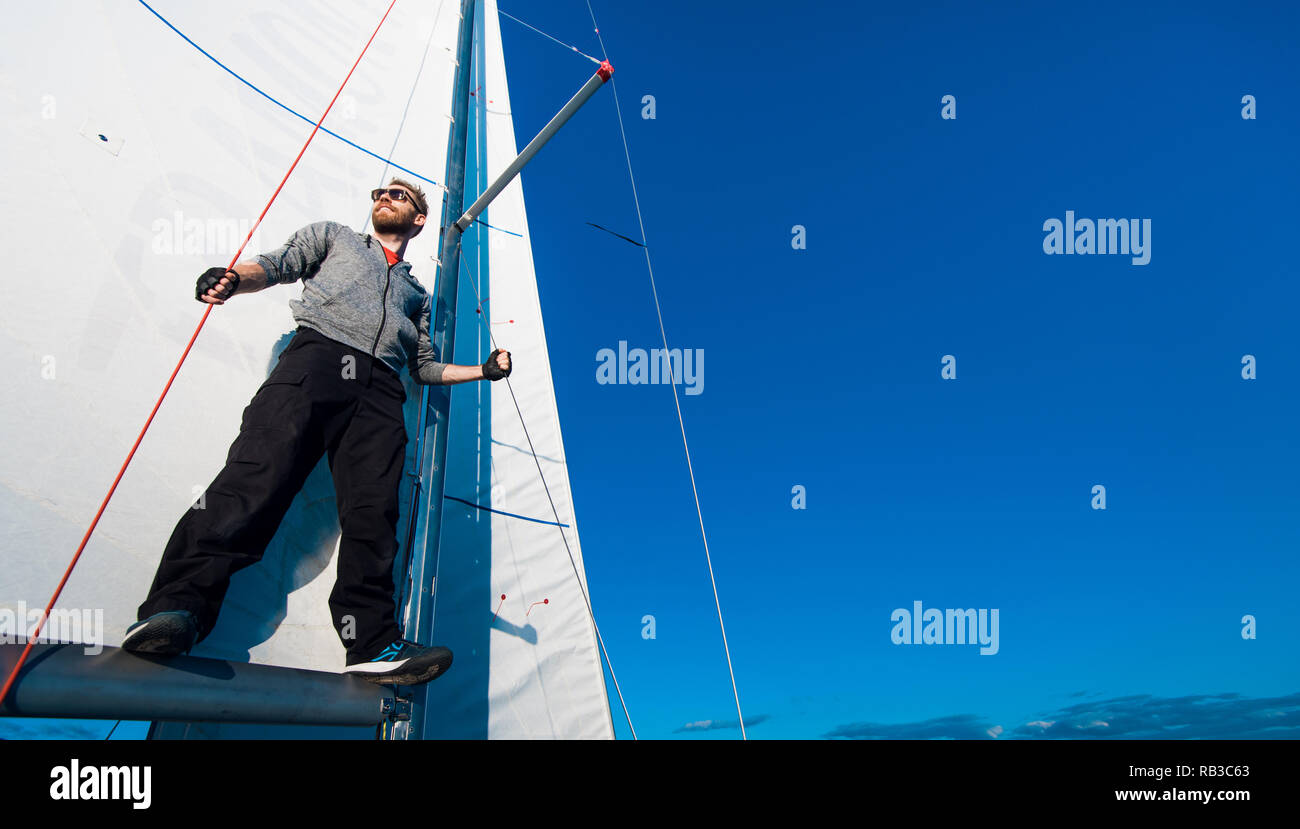 Capitaine de yacht avec une barbe se tient sur la rampe de la voile sur un yacht à voile, tenant la corde dans sa main et souriant, heureux. Yachtsman adultes voyageant à travers le monde. Copy space Banque D'Images