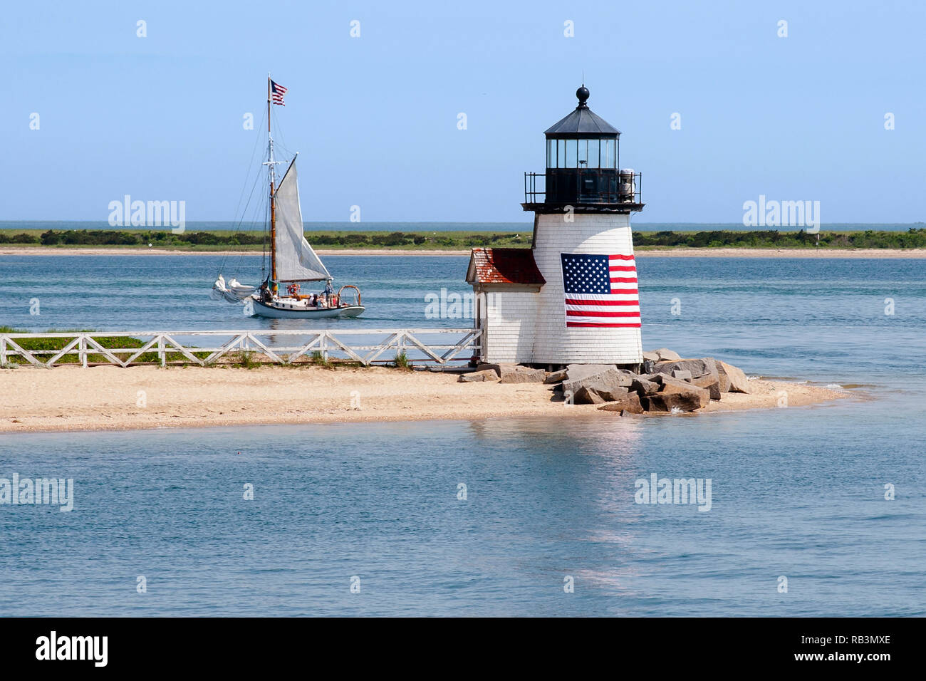 Brant Point Lighthouse, avec son drapeau américain enroulé autour de sa tour en bois, guides un voilier hors de port de l'île de Nantucket dans le Massachusetts. Banque D'Images