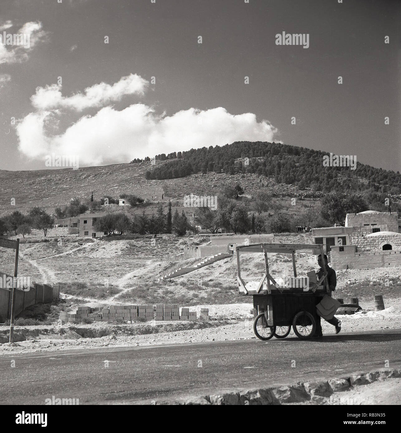 Années 1950, Jersulaem, vendeur de rue avec quatre roues panier, marcher le long de la route à l'extérieur de la ville, Israël Banque D'Images