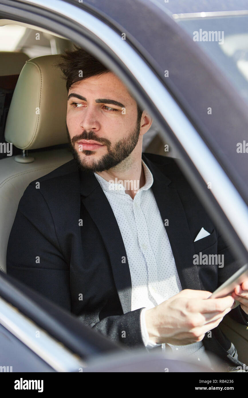 L'homme d'affaires réfléchie en voyage d'affaires à l'aide de l'ordinateur tablette dans la voiture Banque D'Images