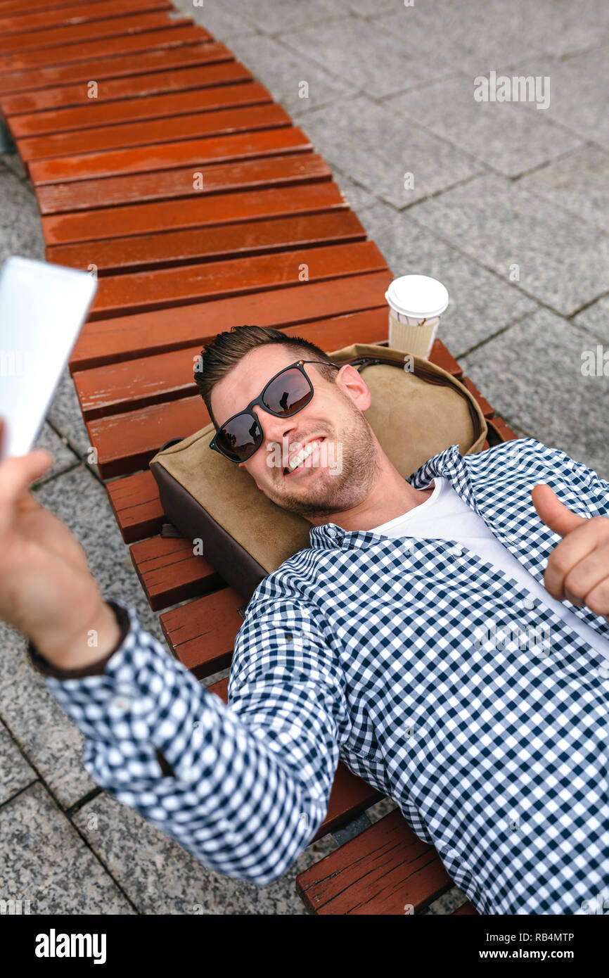 L'homme couché sur un banc de parc de décisions avec mobile selfies Banque D'Images