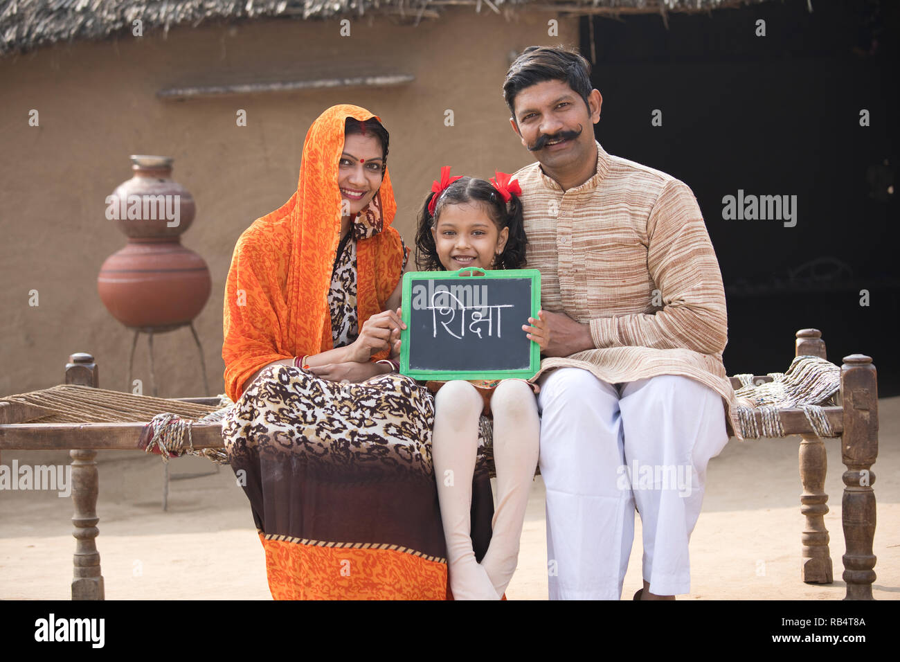 Heureux parents indiens avec daughter holding slate, assis sur un lit traditionnel dans le village Banque D'Images