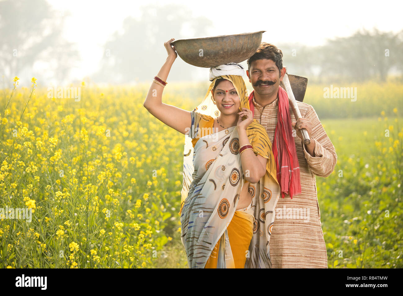 Couple de l'Inde rurale avec poêle de fer et binette dans le colza champ agricole Banque D'Images