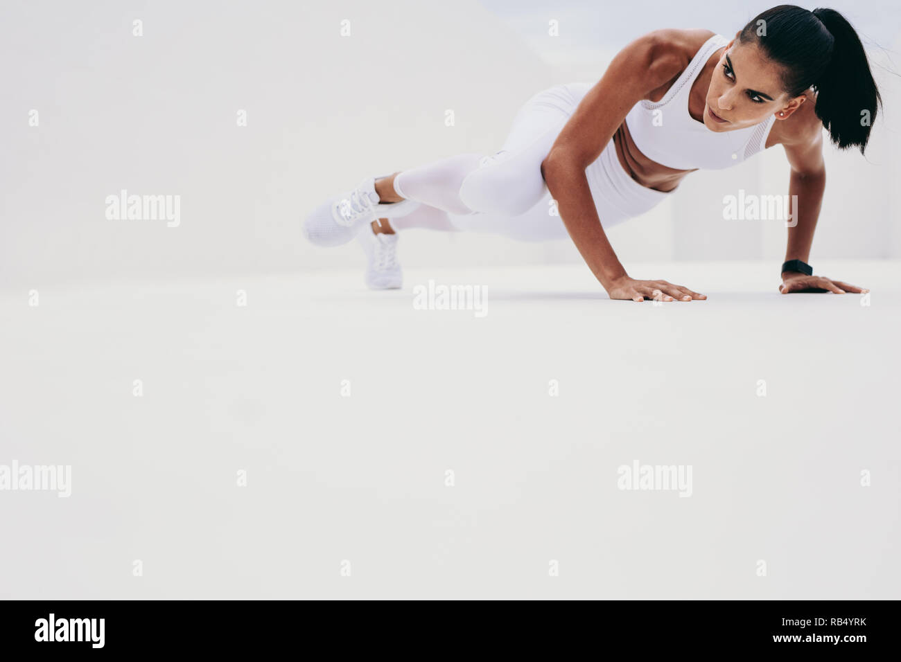 femme de fitness soulevant une jambe tout en faisant des pompes. Femme en vêtements de fitness faisant de l'entraînement. Banque D'Images