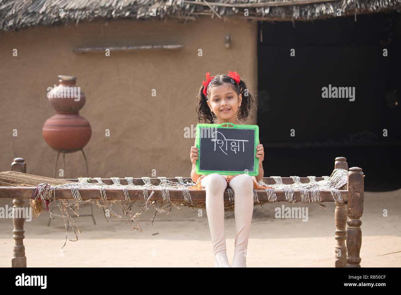 Little Indian girl holding slate, assis sur un lit traditionnel dans le village Banque D'Images