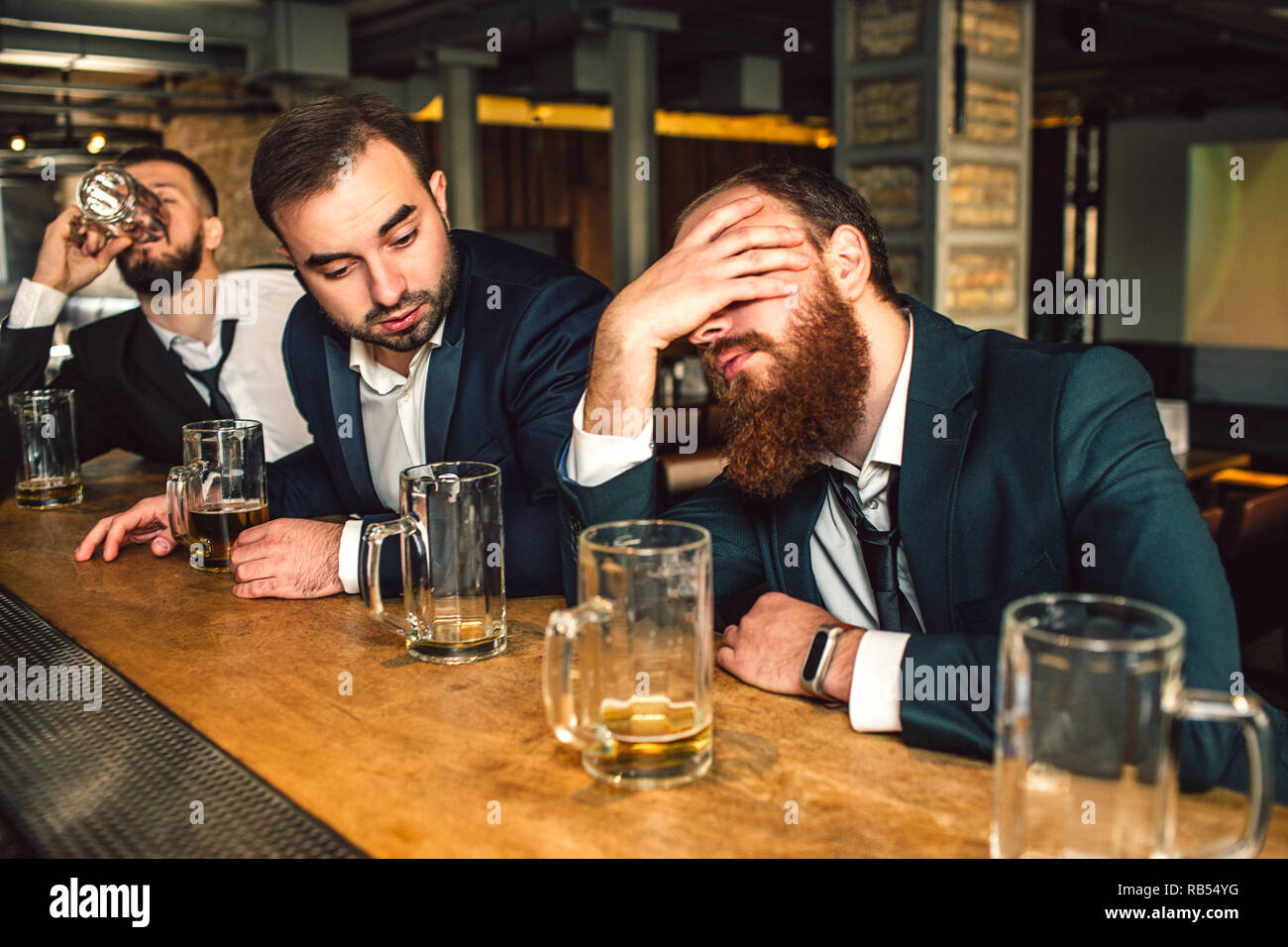 Jeune homme barbu assis devant et le sommeil. Il est ivre. Deuxième jeune homme le regarder. Troisième verre de bière. Banque D'Images