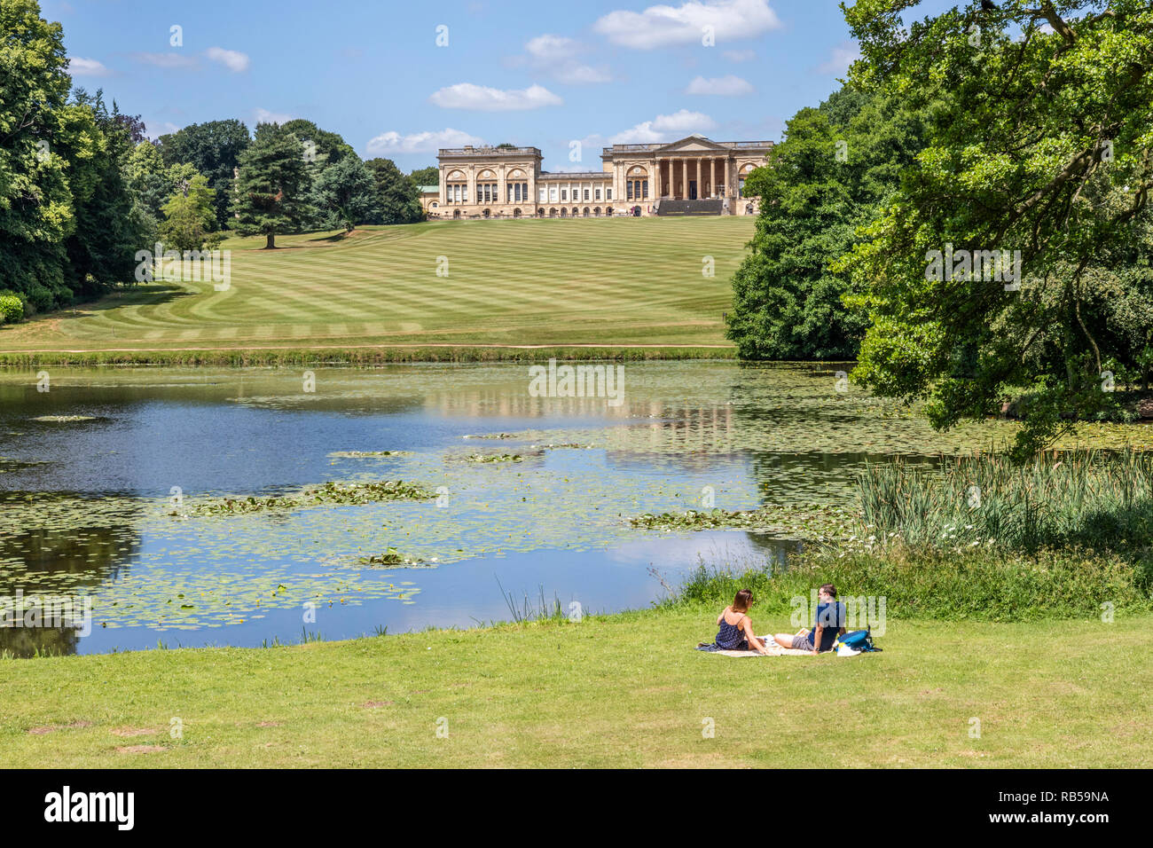 Un jeune couple appréciant un pique-nique au bord du lac à Stowe House Gardens, Buckinghamshire UK Banque D'Images