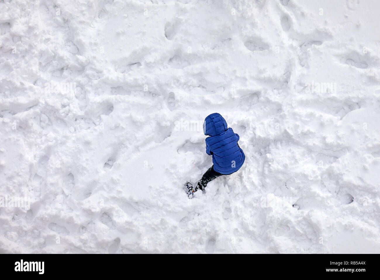 Vue aérienne au-dessus d'un petit garçon face à l' arrière avec manteau bleu jouer dans la neige Banque D'Images
