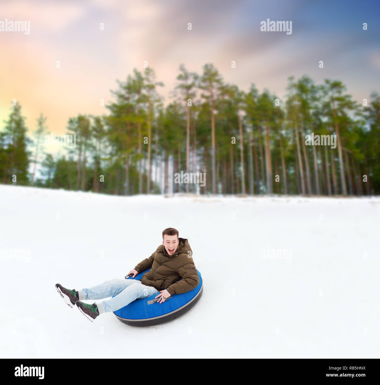 Heureux jeune homme glisser en bas de la colline sur snow tube Banque D'Images