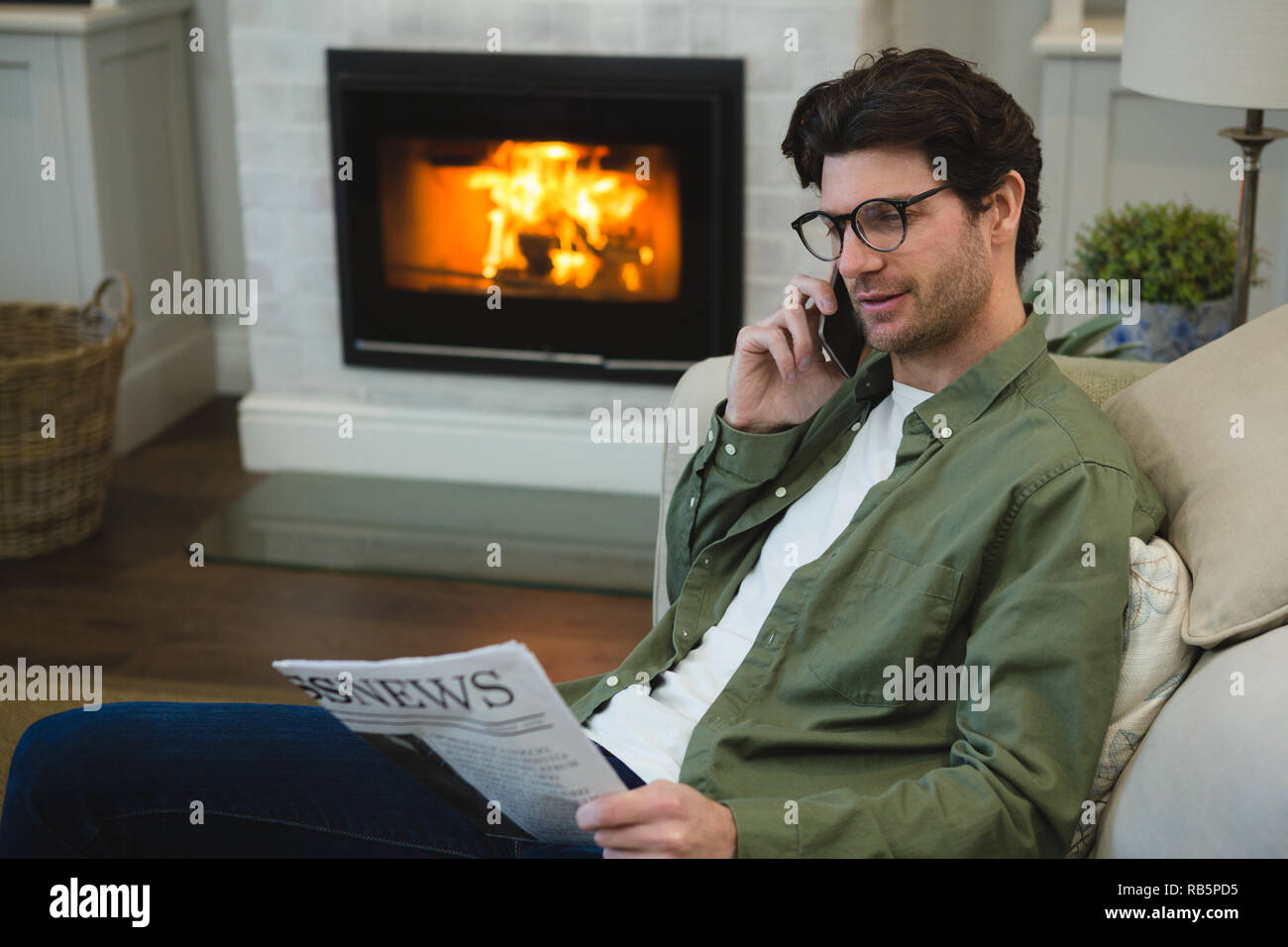 Man reading newspaper while talking on mobile phone Banque D'Images