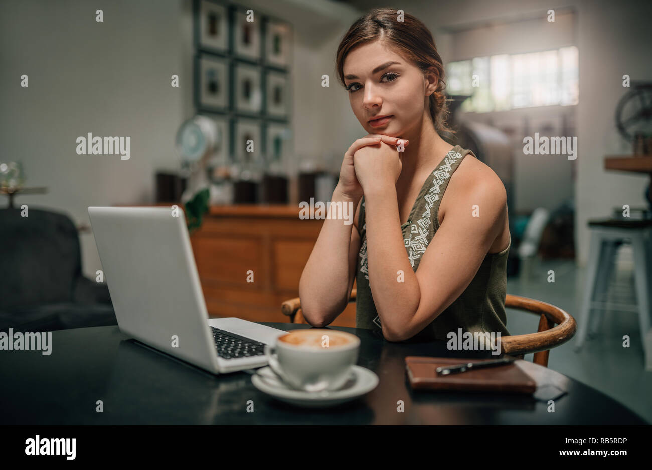 Portrait d'une belle jeune femme la génération z assis dans un café avec son ordinateur portable et ordinateur portable, les yeux dans l'appareil photo Banque D'Images