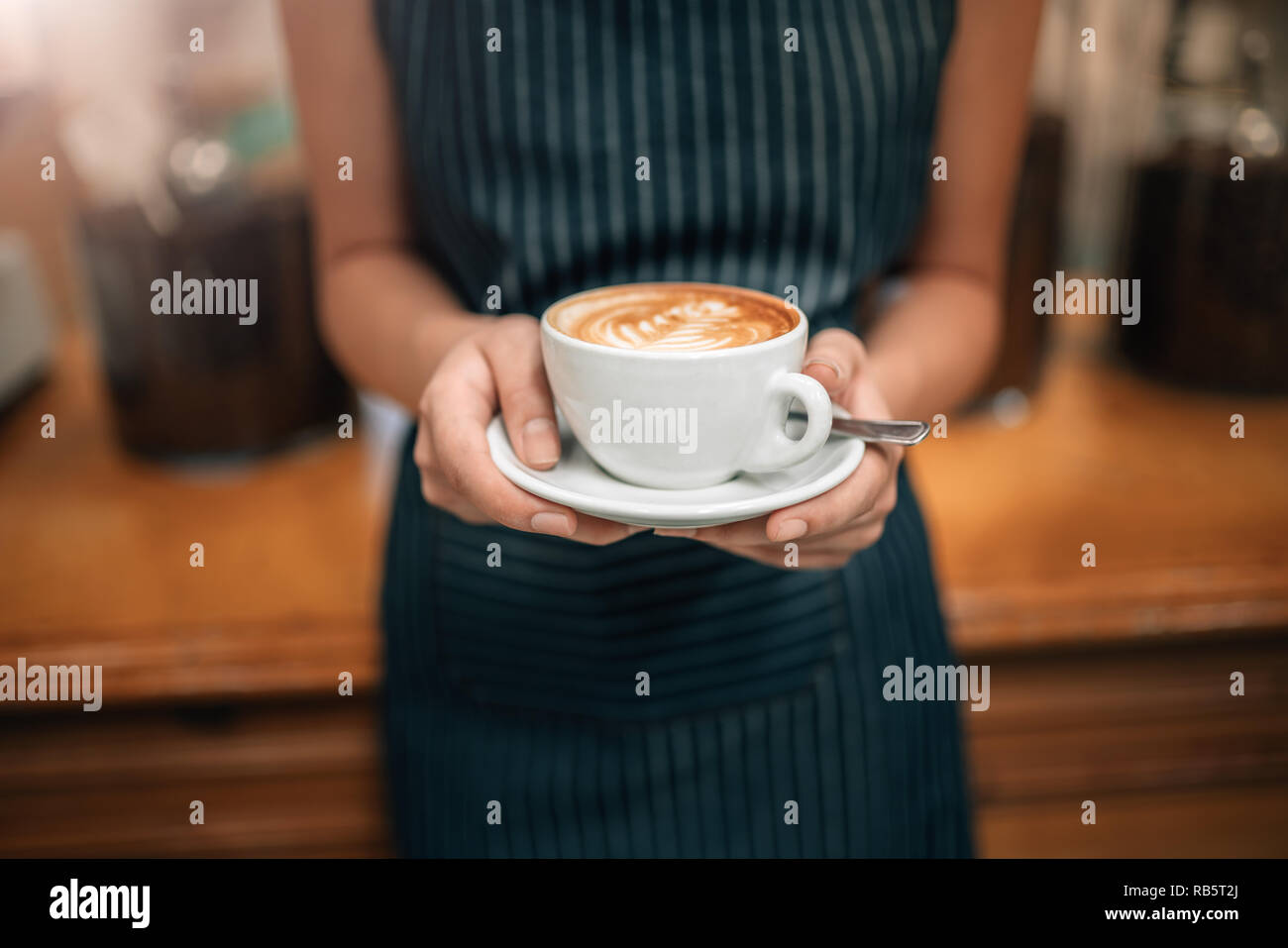 Close up of a waitress holding a coulé bien coffeeCropped Close up de femmes servant du café avec latte art tout en se tenant dans un coffee shop. L'accent sur fe Banque D'Images