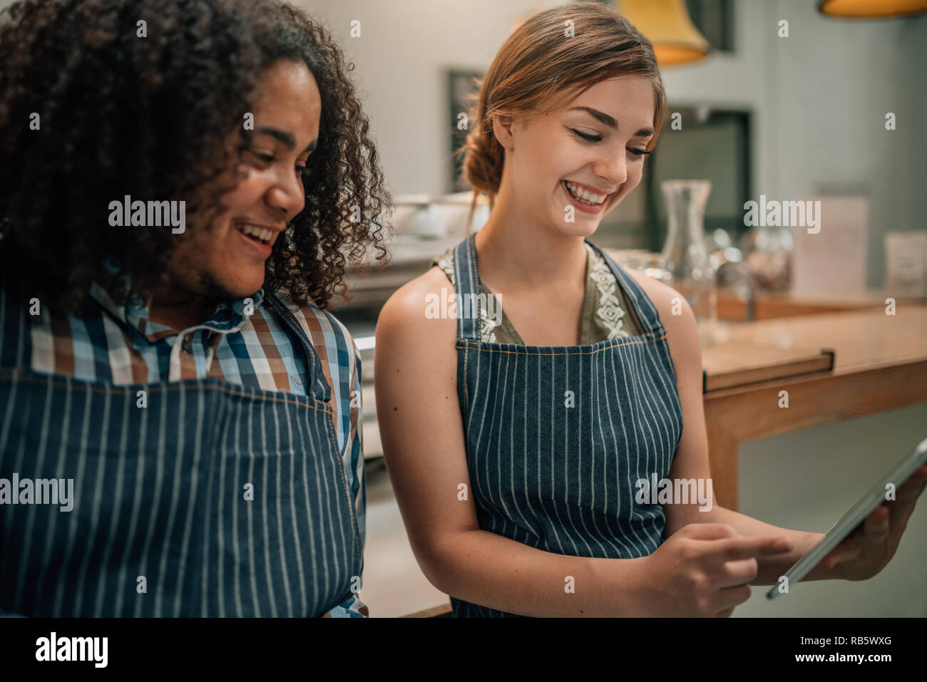 Deux serveurs sourire et rire à quelque chose d'être souligné sur une tablette numérique Banque D'Images
