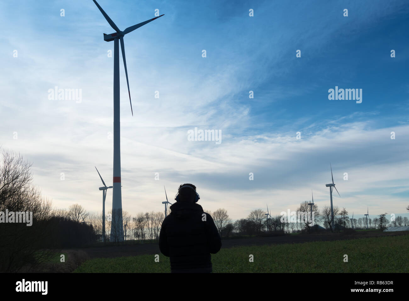 L'homme en face d'une ferme éolienne utilise protecteur de bruit pour réduire le bruit de l'éolienne Banque D'Images