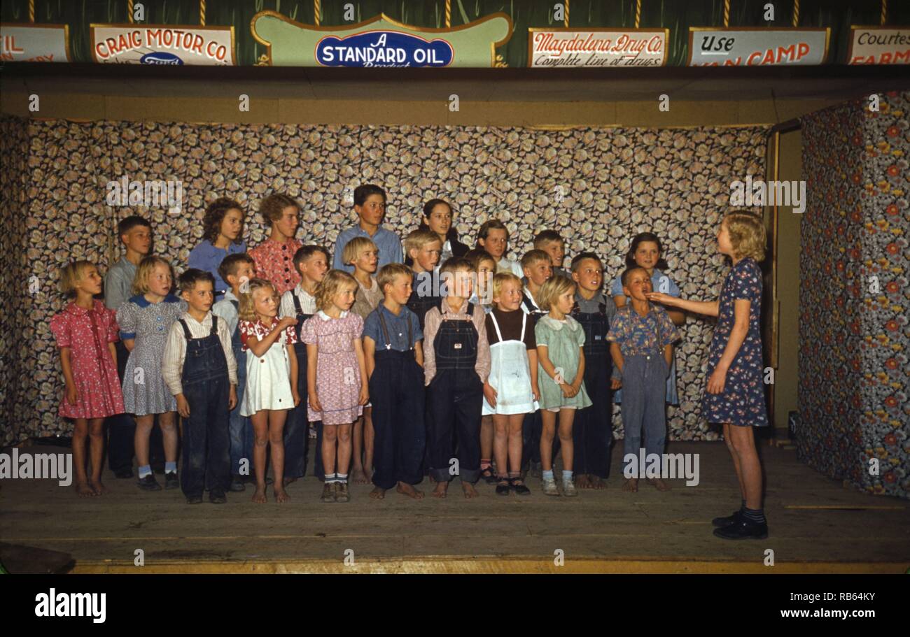 Photographie en couleur de l'école les enfants chantent à Pie Town, Nouveau Mexique. Au-dessus de la scène publicité pour Craig Motor Co., Standard Oil, et Magahalena Drug Co. sont visibles. Datée 1940 Banque D'Images