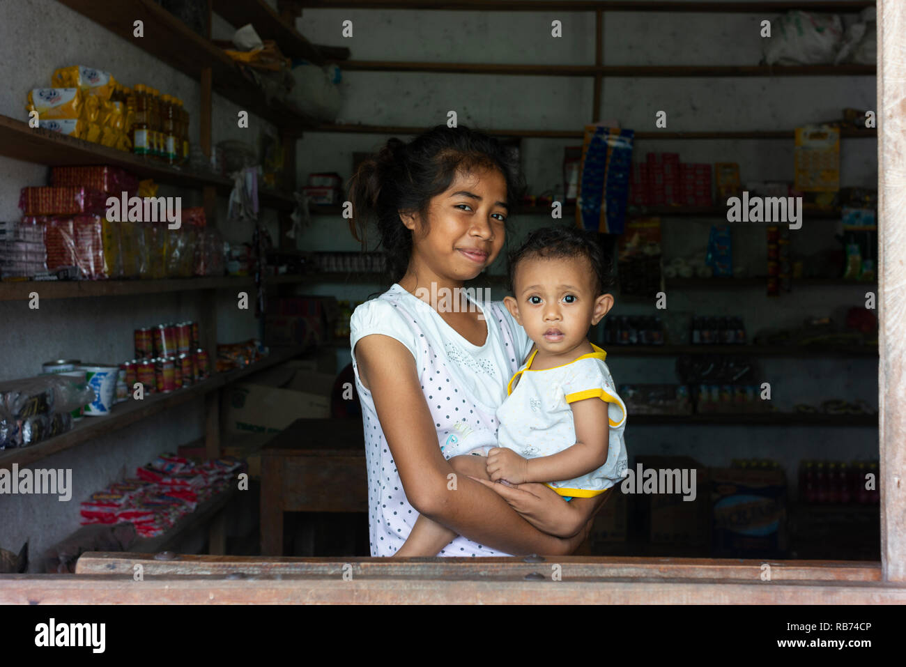 Une jeune femme tient son jeune frère dans une petite boutique de Natarbora sur la côte sud du Timor Leste. Banque D'Images