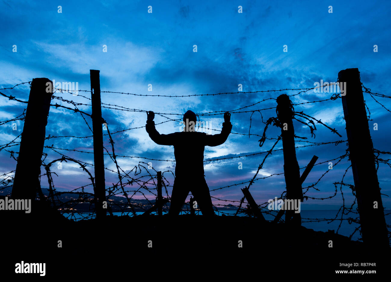 Silhouette of man looking through Barbed Wire/ le fil barbelé clôture à la nuit. Brexit, immigration, asile concept... Banque D'Images