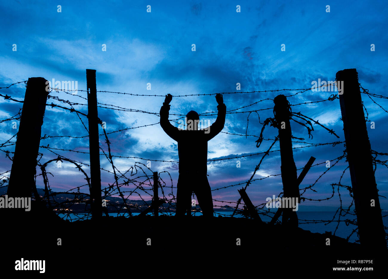 Silhouette of man looking through Barbed Wire/ le fil barbelé clôture à la nuit. Brexit, immigration, asile concept... Banque D'Images