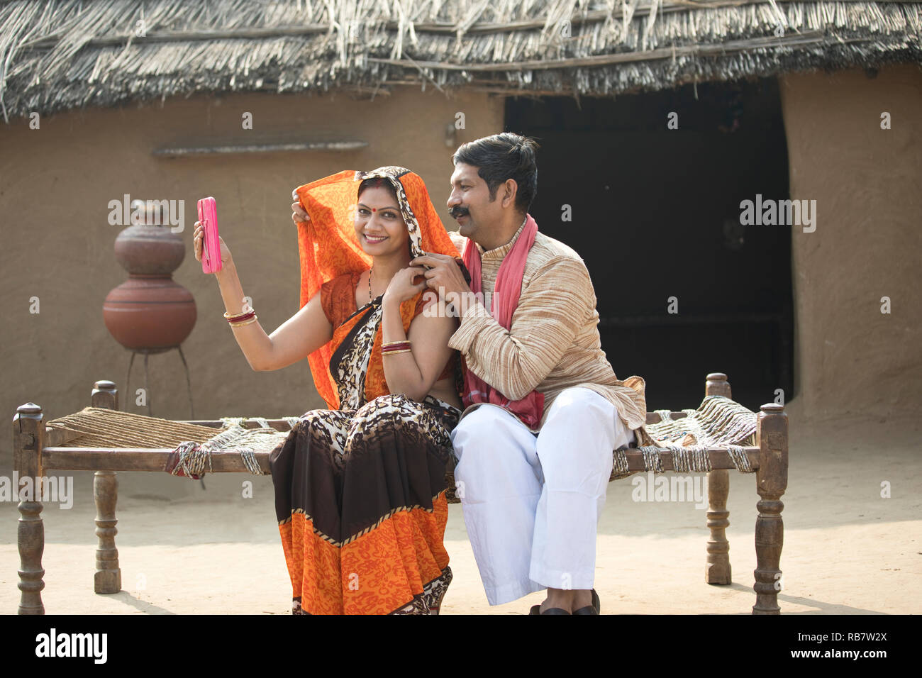 Couple à la recherche de l'Inde rurale en miroir tandis qu'assis sur un lit traditionnel dans le village Banque D'Images