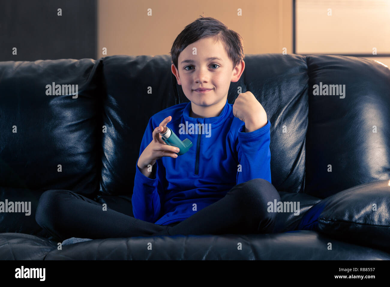 8 ans portant des vêtements sportifs souffrant d'asthme inhalateur assis dans le canapé avec poing serré. Concepts : la santé, la maladie, le dopage Banque D'Images