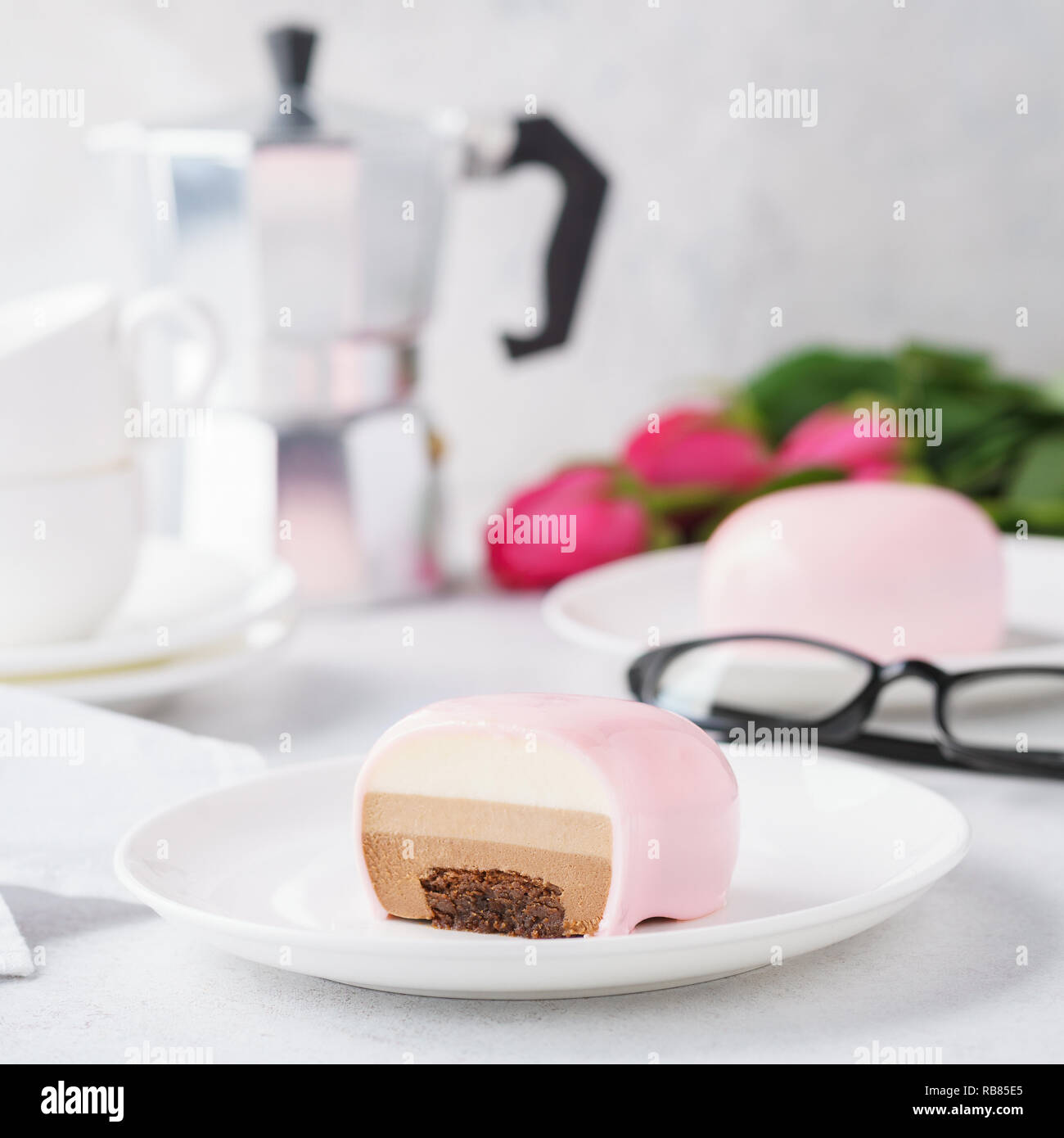 Trendy gâteaux mousses avec mirror glaze rose. Gâteries en forme de coeur pour la Saint-Valentin. Fleurs dans l'arrière-plan. Banque D'Images