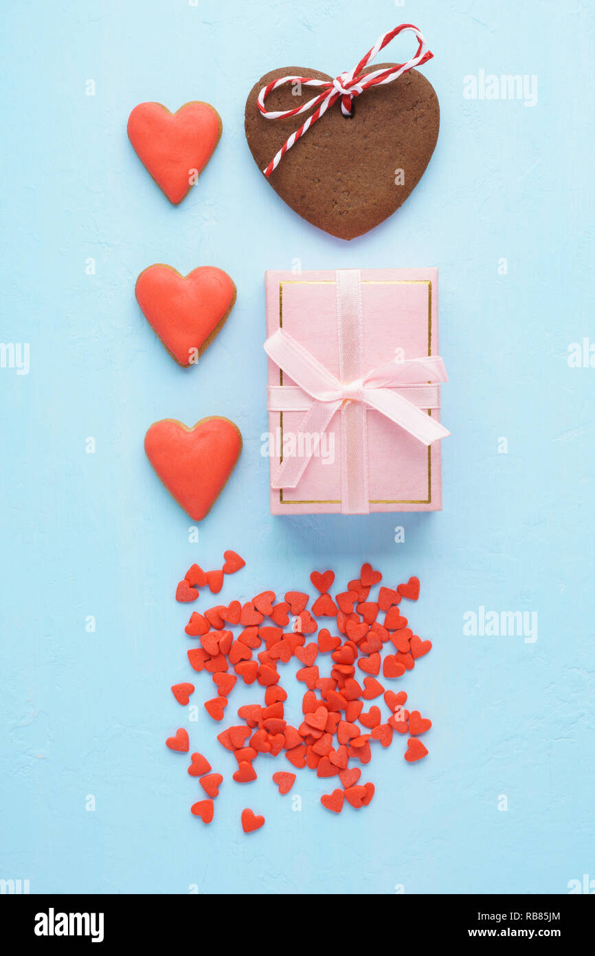 Saint-valentin conception mise en page créative. Boîte-cadeau avec ruban rouge en forme de coeur, cookies, meringues et bonbons. Les couleurs bleu et rose pastel. Mise à plat. Banque D'Images