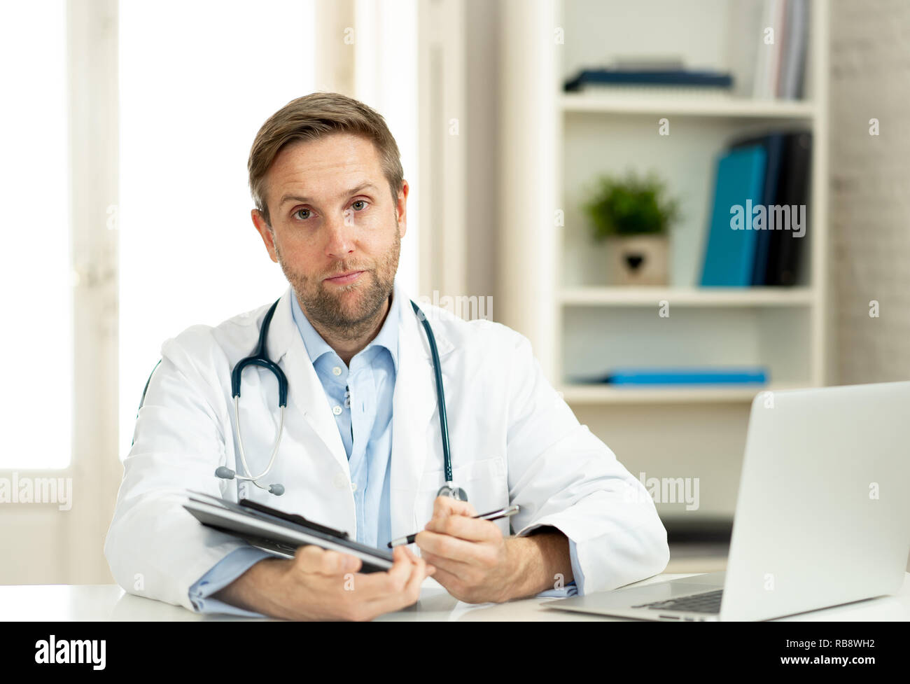 Portrait of handsome doctor working on laptop in hôpital clinique bureau avec naturel dans les soins professionnels et médicaux Banque D'Images