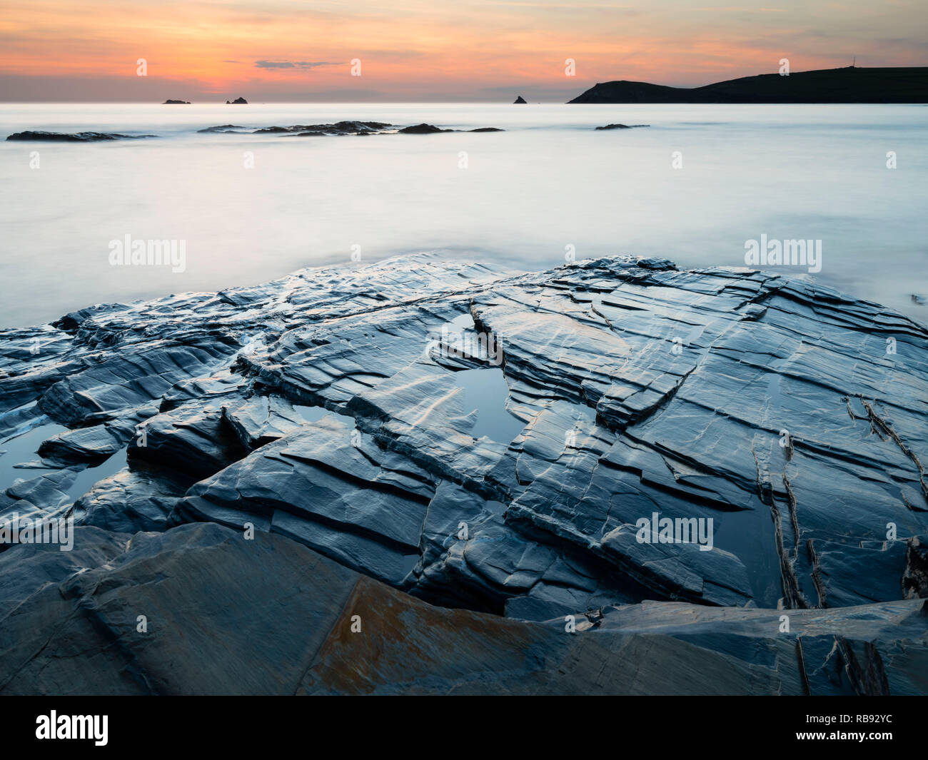 Une vue de Constantine Bay dans la région de North Cornwall, England UK au crépuscule et à marée haute à l'ardoise des roches dans l'avant-plan. Banque D'Images