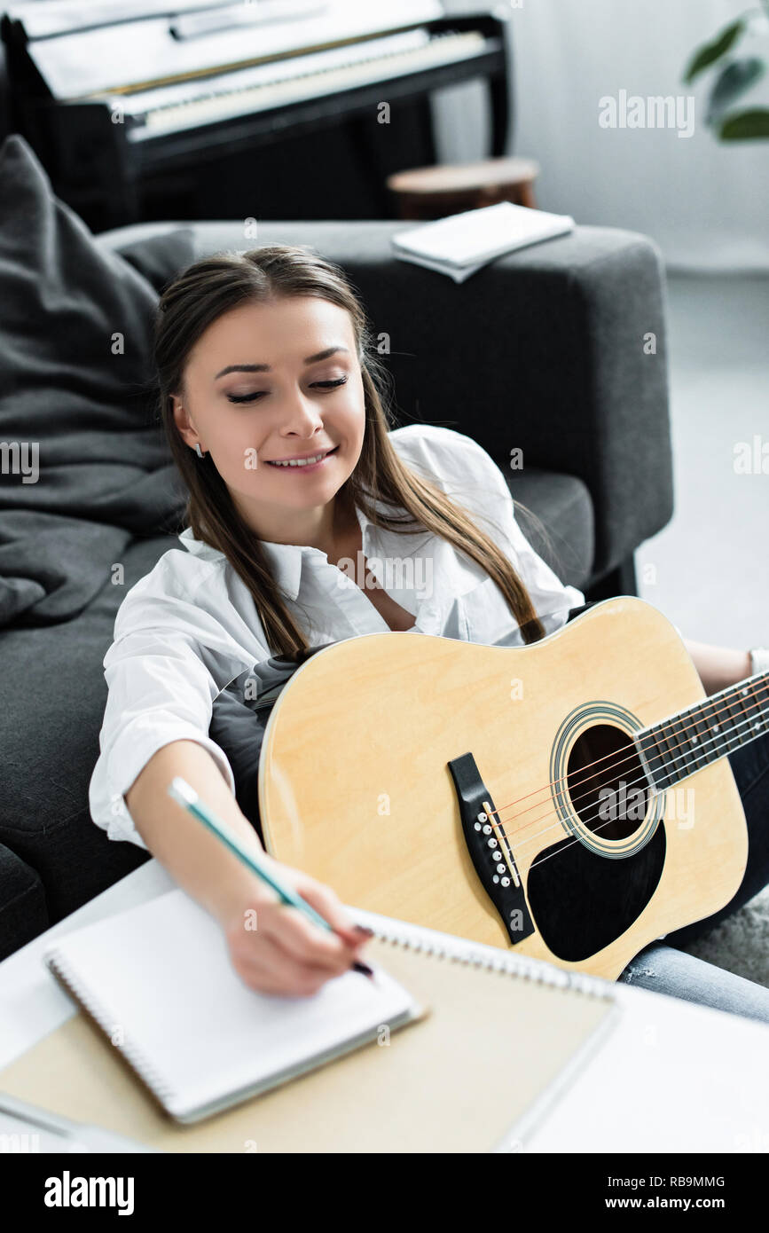 Smiling girl avec guitare acoustique écrit dans l'ordinateur portable tout en composant la musique à la maison Banque D'Images