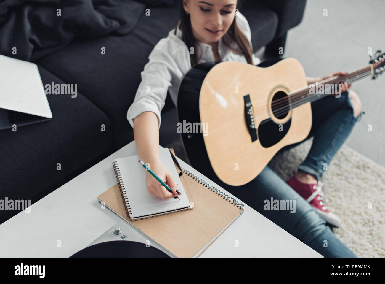 Fille avec guitare acoustique assis sur le plancher et l'écriture dans l'ordinateur portable tout en composant la musique à la maison Banque D'Images