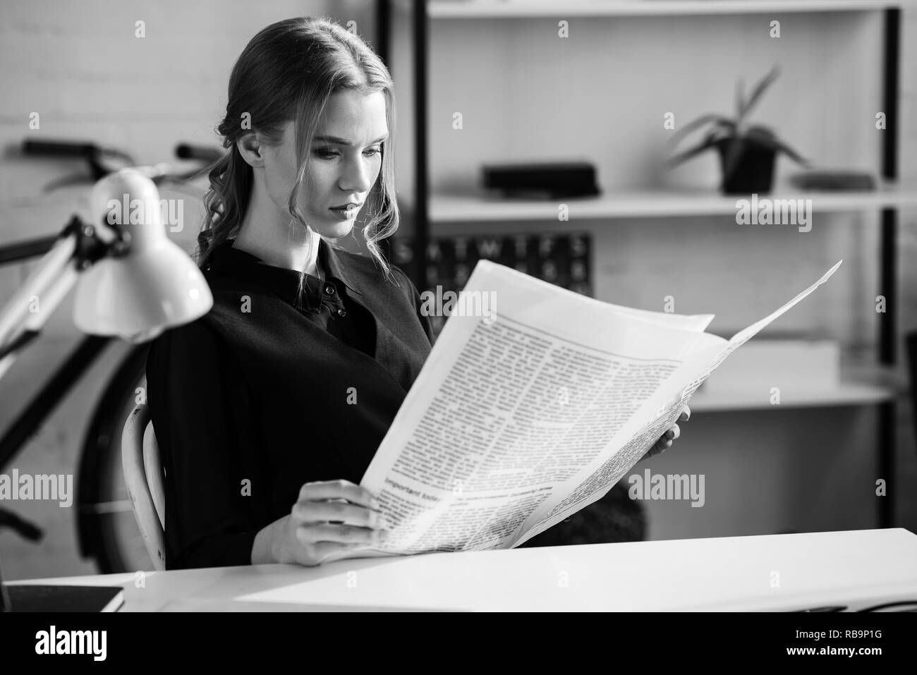 Photo noire et blanche de man dans l'usure formelle sitting at desk et lisant le journal sur le lieu de travail Banque D'Images