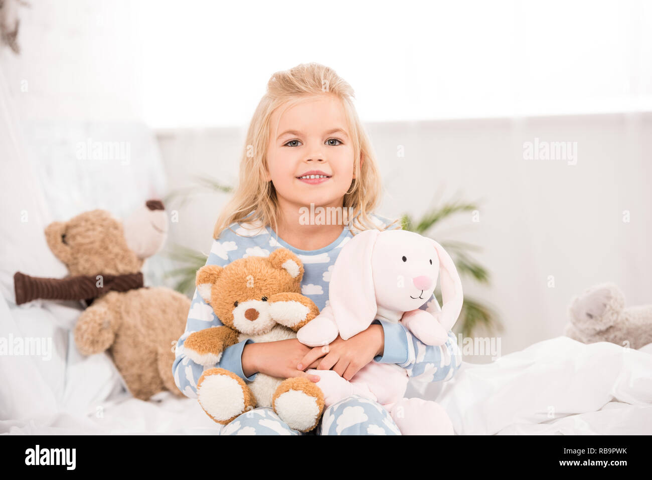 Smiling adorable enfant assis avec des jouets mous on bed Banque D'Images