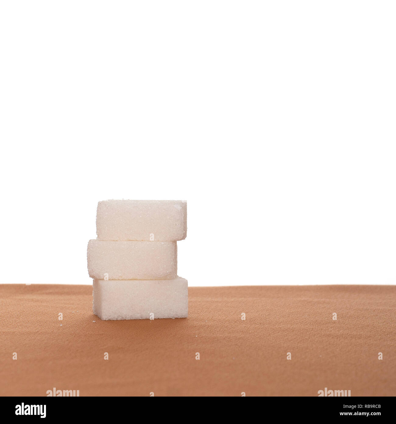 Pile de trois morceaux de sucre sur les tissus, le fond blanc. L'alimentation saine. Banque D'Images