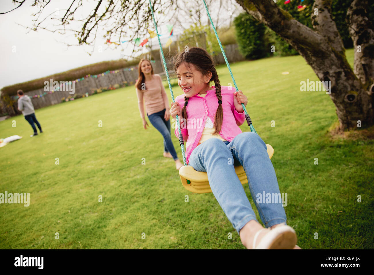 Petite fille jouant à l'extérieur sur une balançoire alors que son aide à sa mère et la pousse. Elle a l'amusement et de plaisir. Banque D'Images