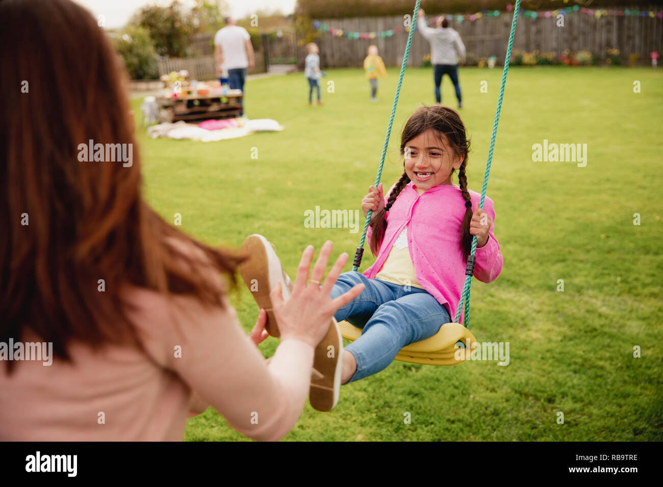 Petite fille jouant à l'extérieur sur une balançoire alors que son aide à sa mère et la pousse. Elle a l'amusement et de plaisir. Banque D'Images