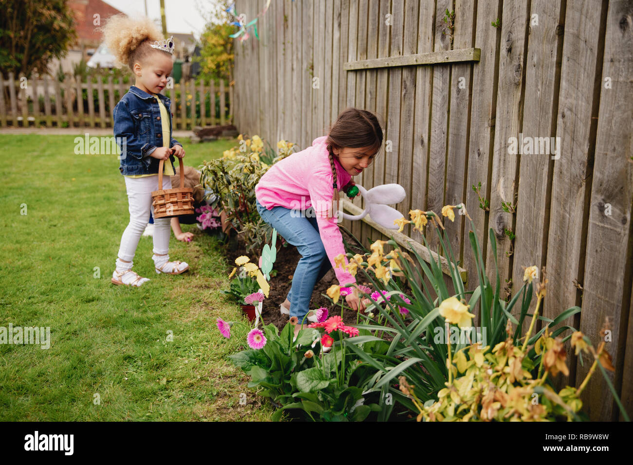 Deux petites filles à la recherche d'oeufs de pâques en chocolat dans le jardin. Ils sont à la recherche dans le lit de fleur, à côté les jonquilles. Banque D'Images