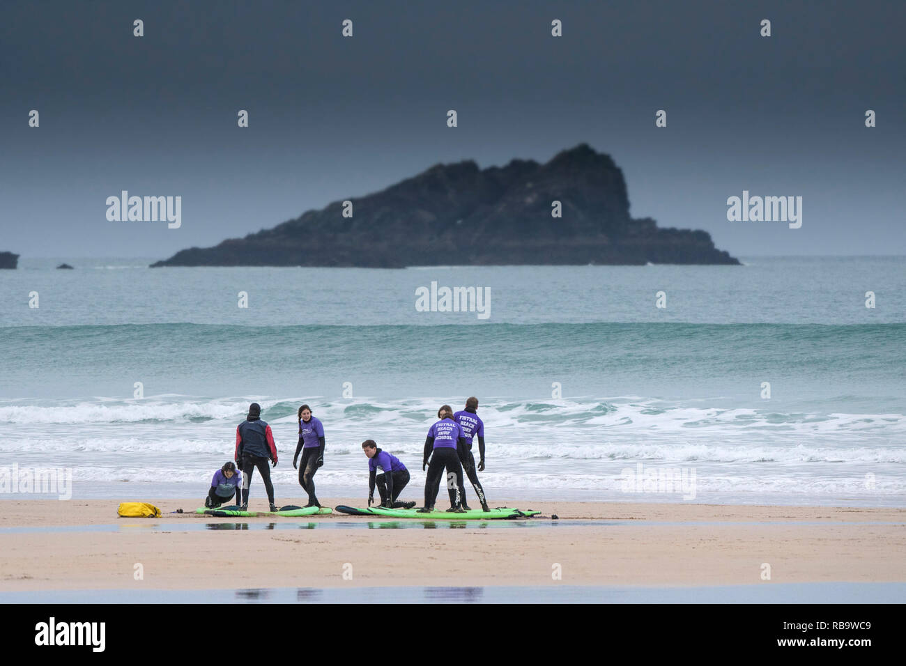 Un groupe de surfeurs débutants ayant une leçon de surf sur la plage de Fistral avec l'île rocheuse appelée la poule à l'arrière-plan. Newquay Cornwall. Banque D'Images