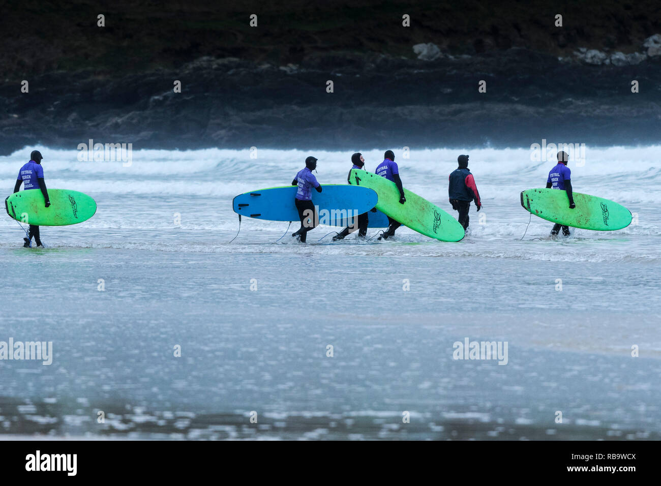 Les surfeurs débutants avec leurs planches de surf et de marcher dans la mer pour une leçon de surf à la plage de Fistral Newquay en Cornouailles. Banque D'Images